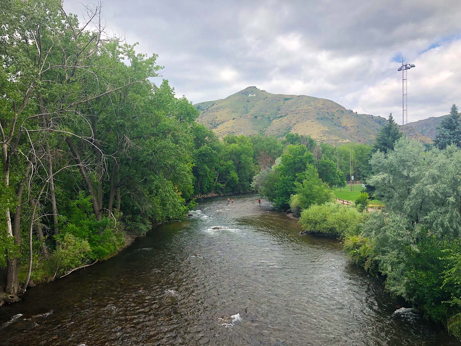 Two anglers fishing Clear Creek town section with mountains and green trees in background